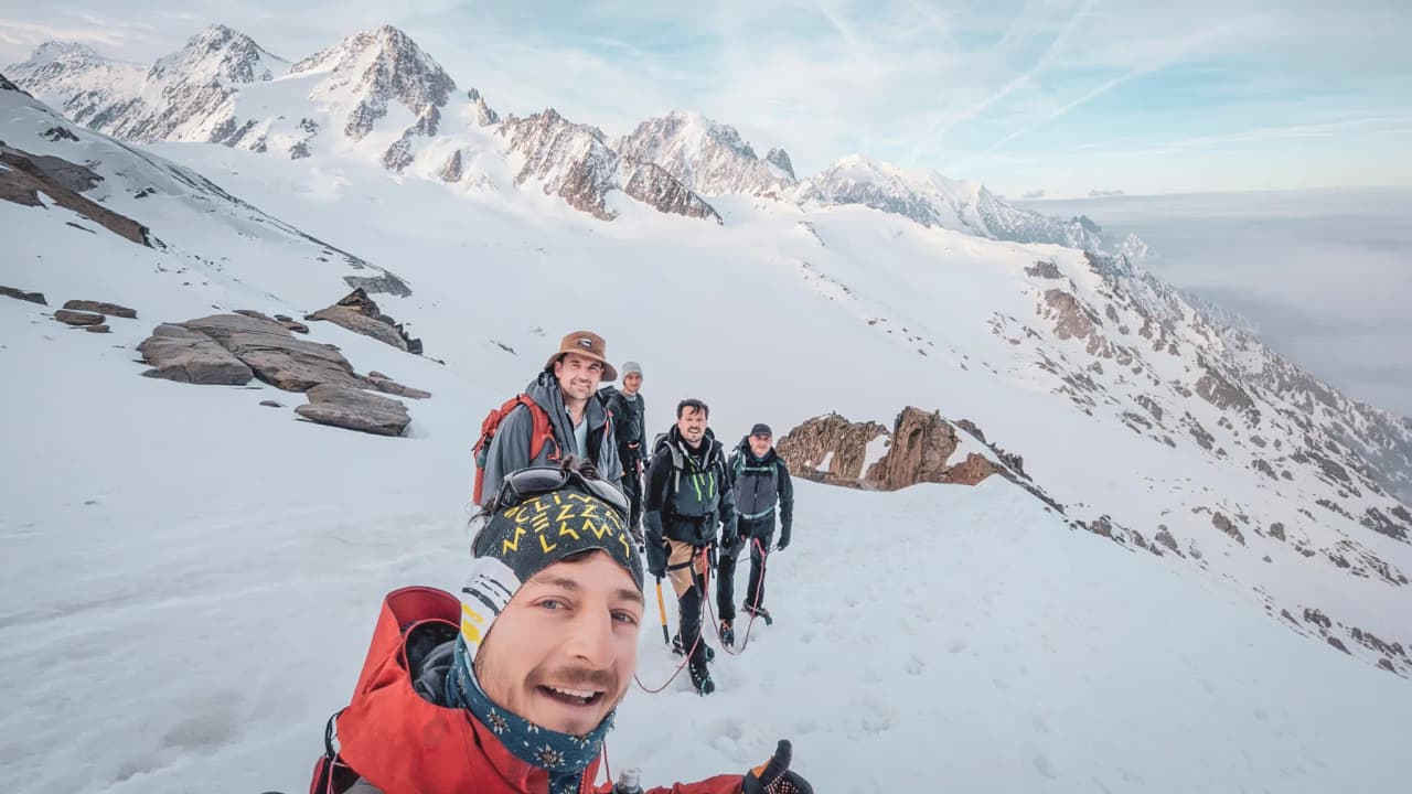 Five smiling hikers in the mountains, surrounded by glaciers and majestic peaks.