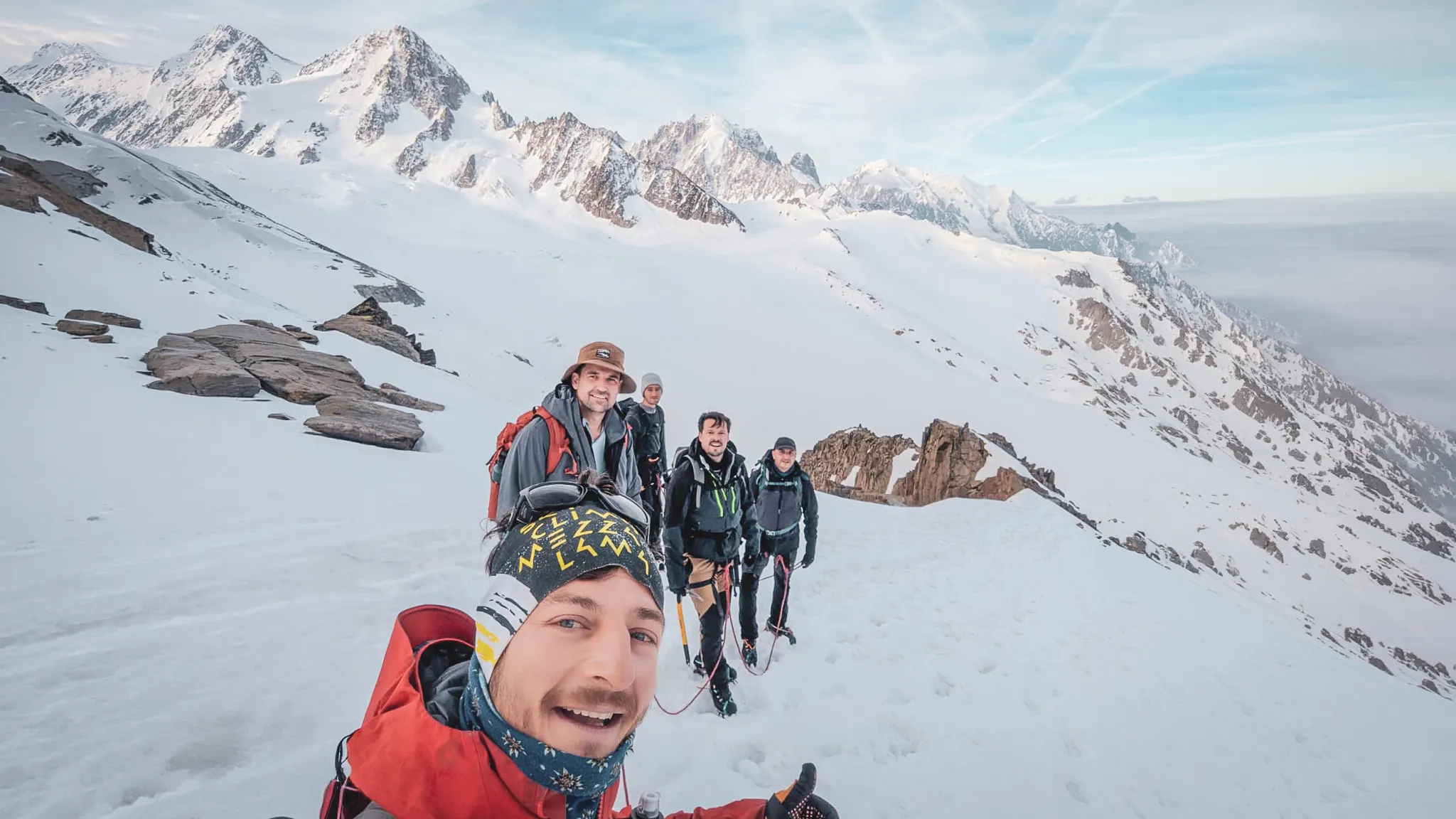 Cinq randonneurs souriants en montagne, entourés de glaciers et de sommets majestueux.