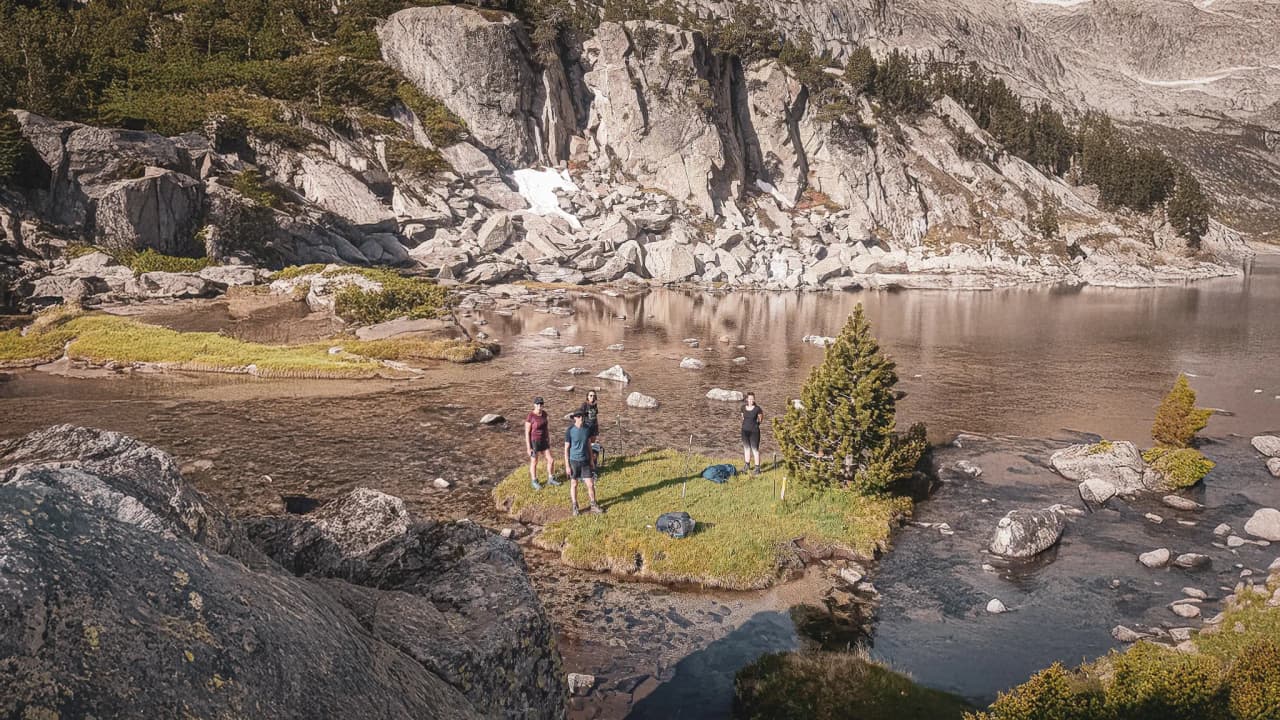 Four hikers on a green island, surrounded by mountains and a serene lake.