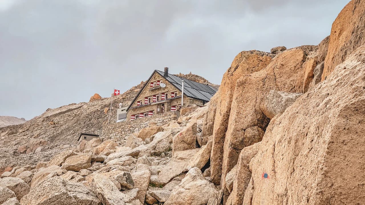 Isolated mountain hut among the rocks, with Swiss flags, in a majestic alpine landscape.