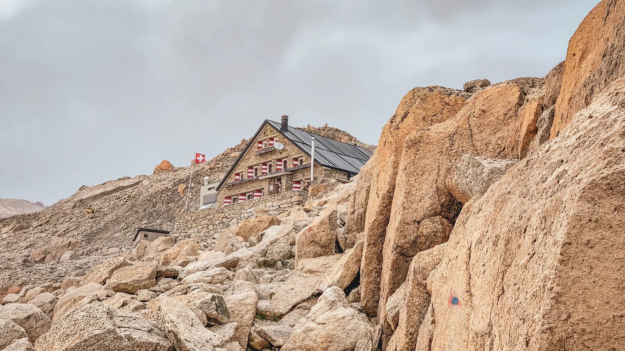 Isolated mountain hut among the rocks, with Swiss flags, in a majestic alpine landscape.