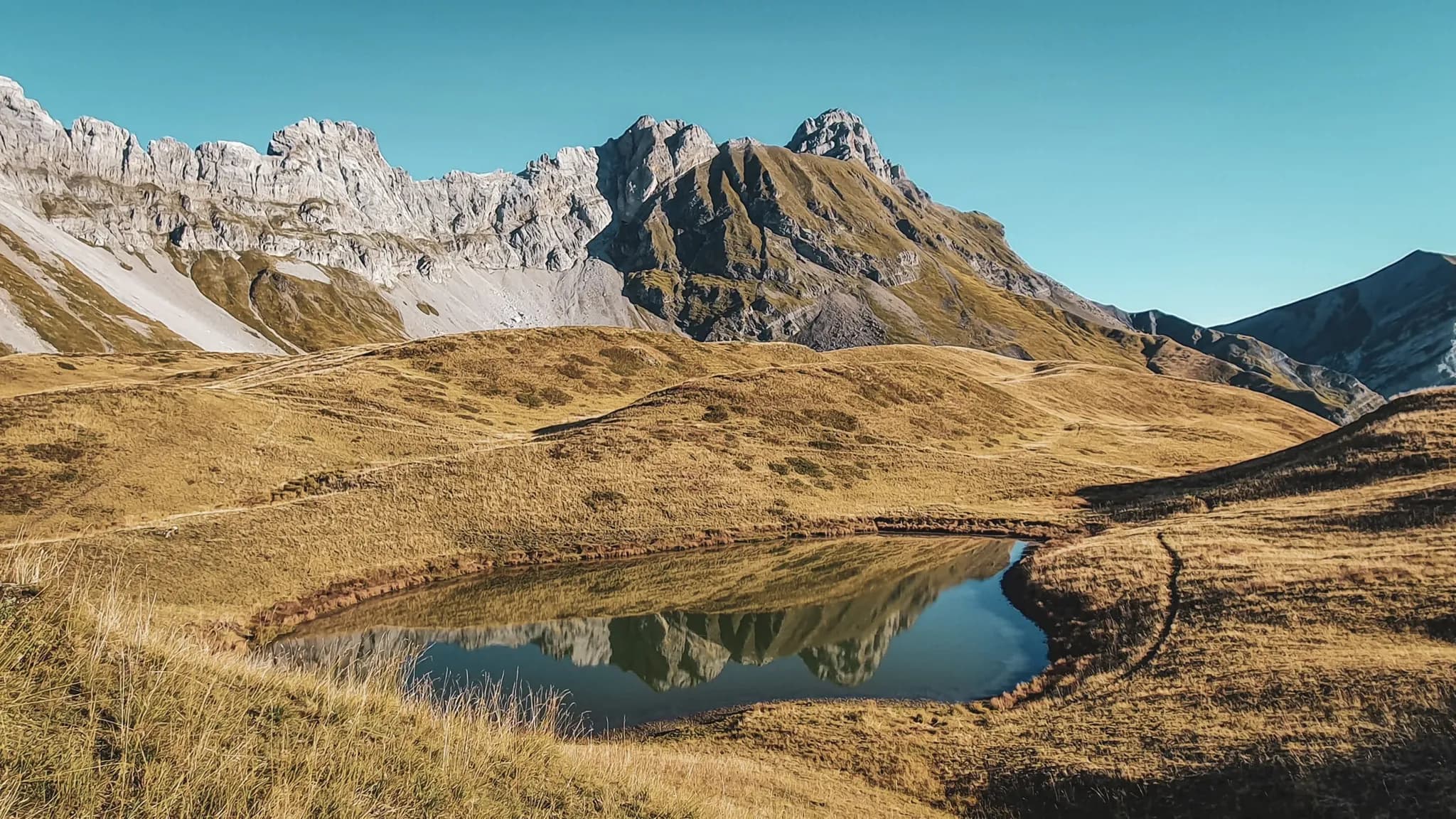 Reflets des sommets des Aravis dans un paisible lac entouré de prairies verdoyantes.