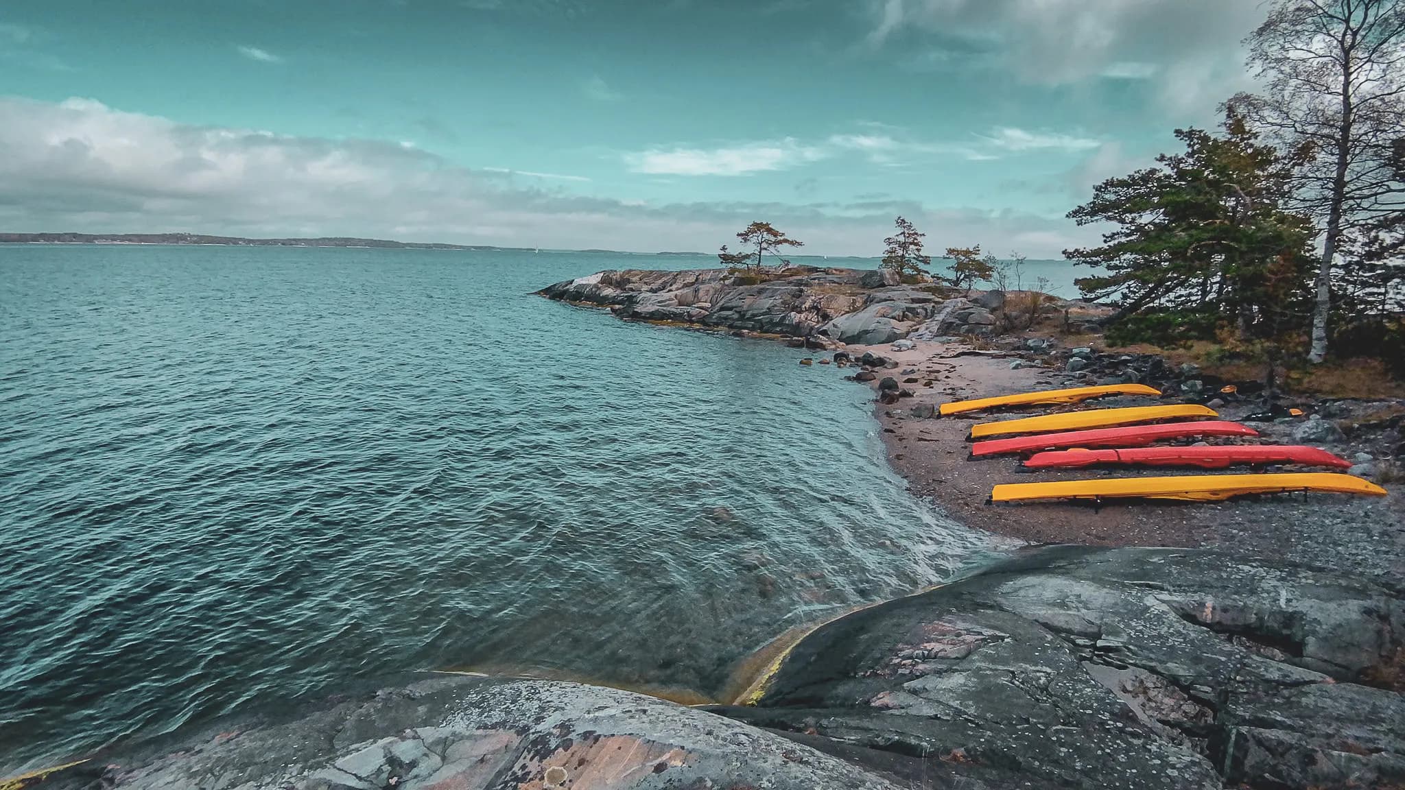 Colourful canoes on a rocky beach, calm water and clear skies, an invitation to archipelago adventure.