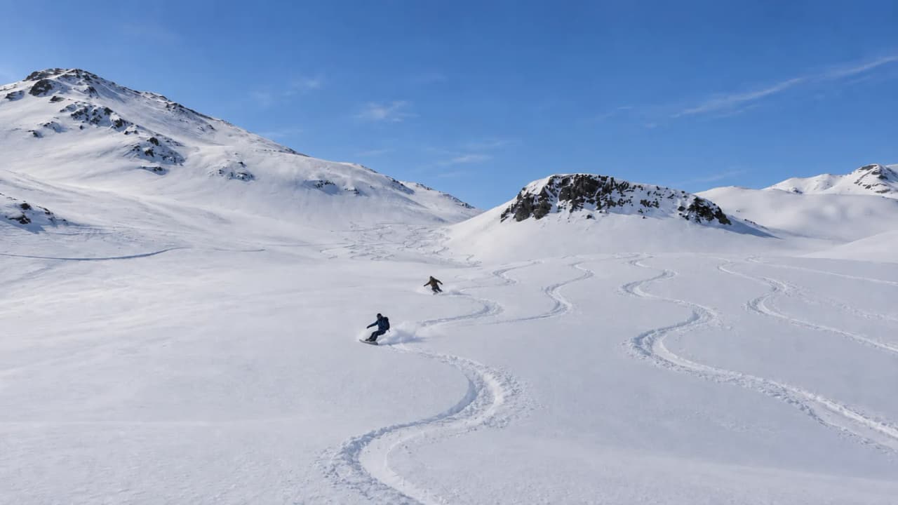 Two people are enjoying splitboarding on the pristine snow in the sun-drenched mountains.