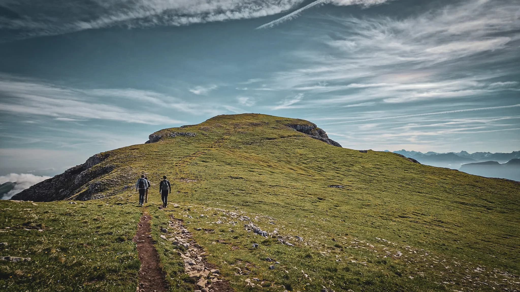 Two hikers are walking along a leafy path leading to Mont Aiguille, under a clear sky.