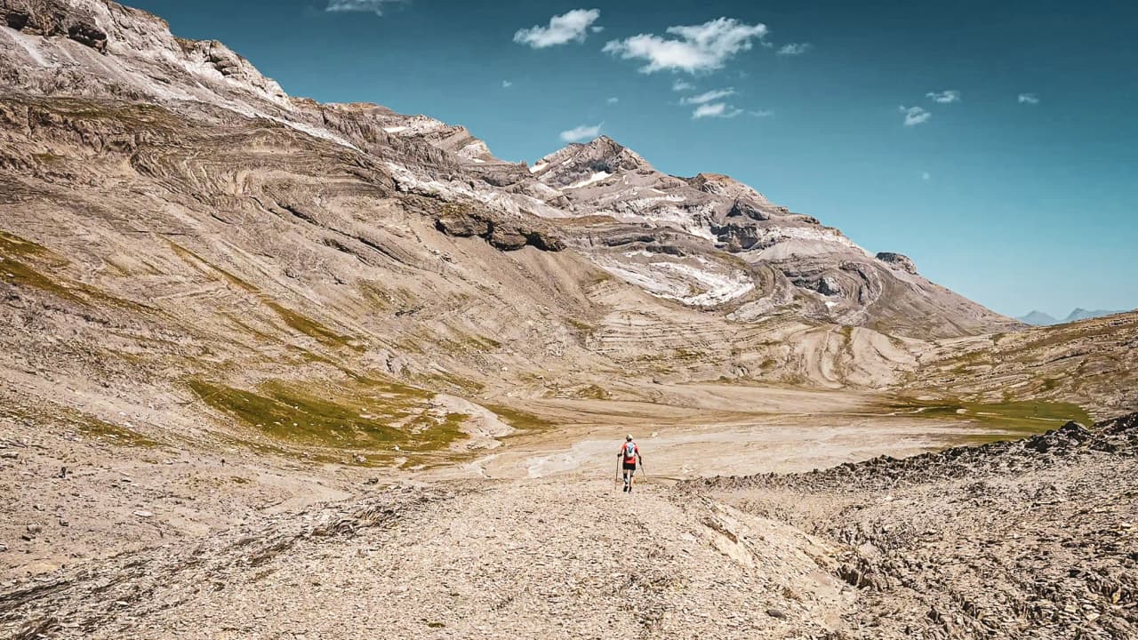 Een eenzame wandelaar baant zich een weg over een bergpad, omringd door majestueuze toppen van de Pyreneeën.