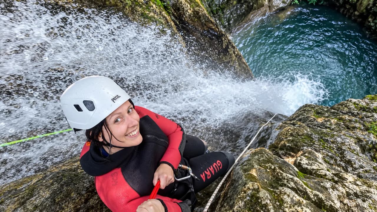 Une aventurière souriante en pleine descente de canyon, entourée d'eau cascada.