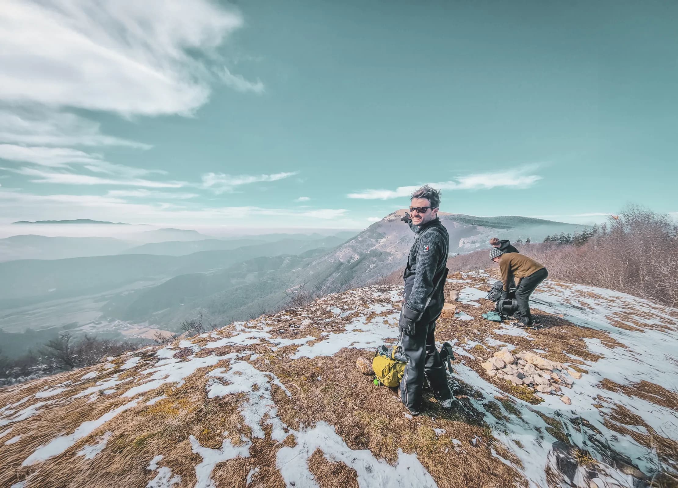 Two adventurers at the top of a mountain, enjoying spectacular scenery under a blue sky.