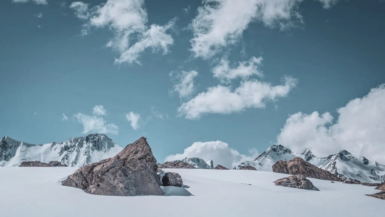 An enchanting alpine landscape with snow-capped mountains and a blue sky dotted with clouds. Come and explore!
