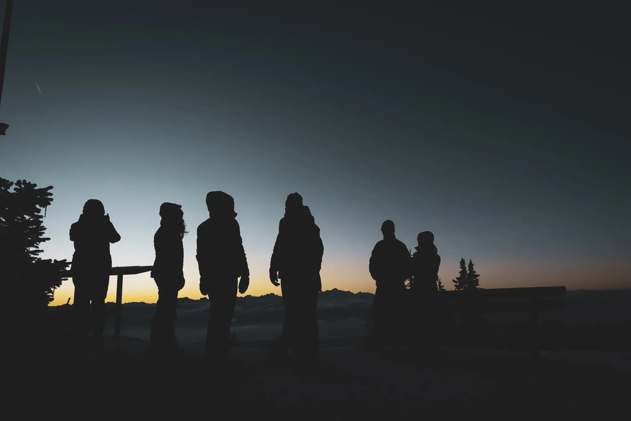 Hikers silhouetted against a sunrise over snow-capped mountains.