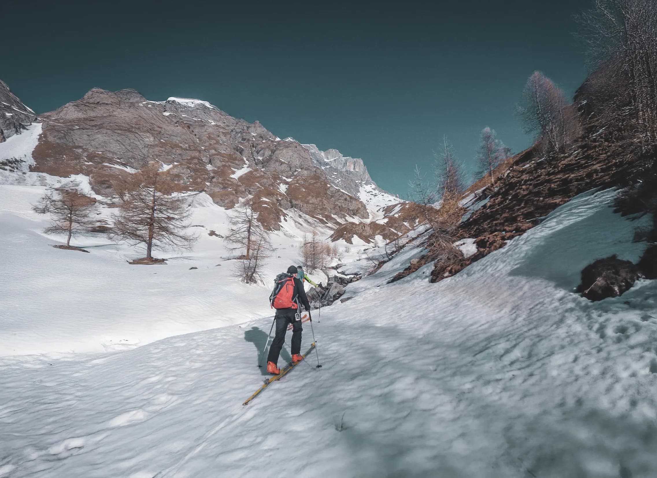 Un skieur en randonnée sur des pentes enneigées, entouré de paysages montagneux majestueux.