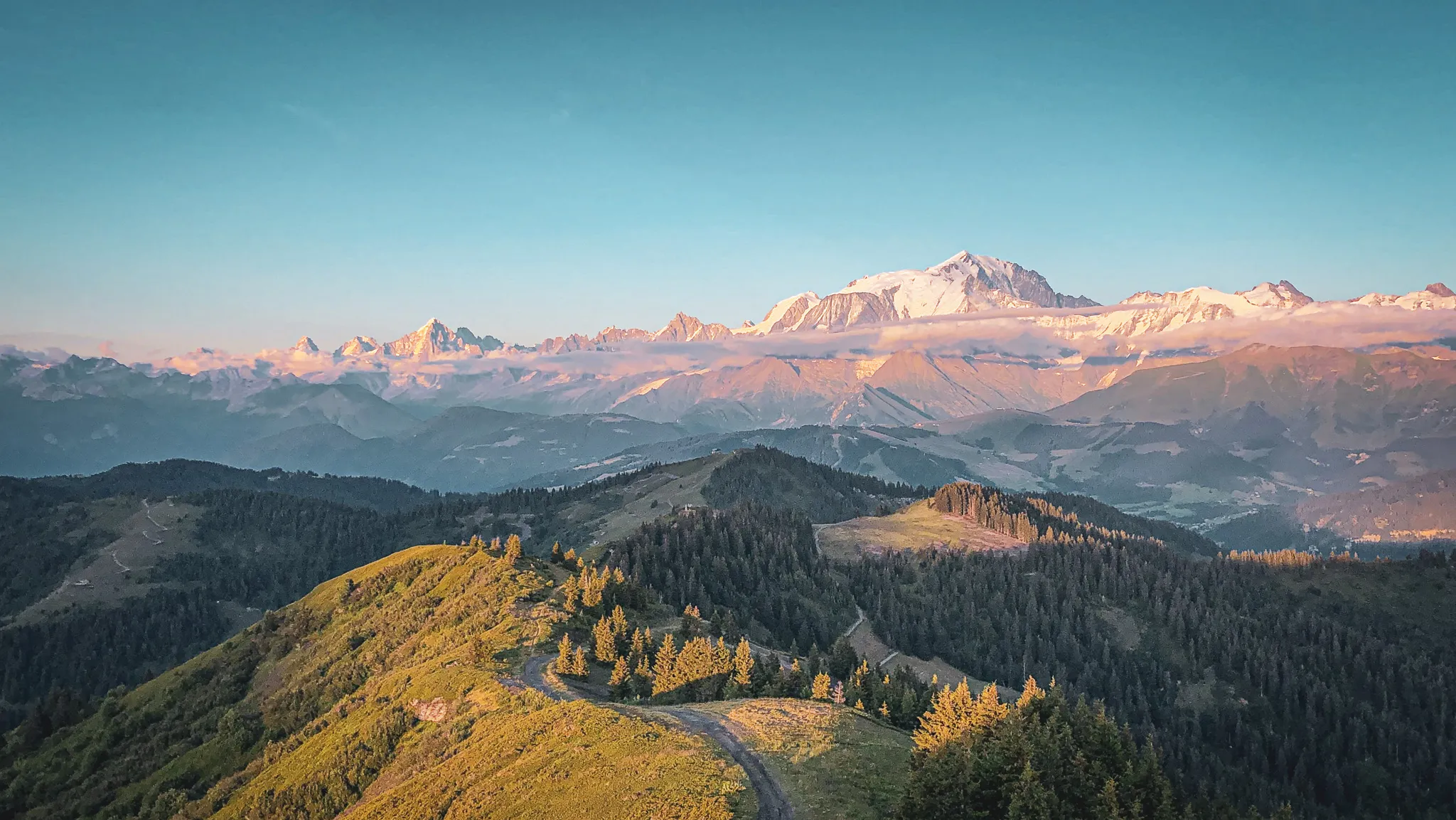 Vue panoramique des montagnes alpines, avec le Mont-Blanc majestueux au loin, illuminé par le soleil.
