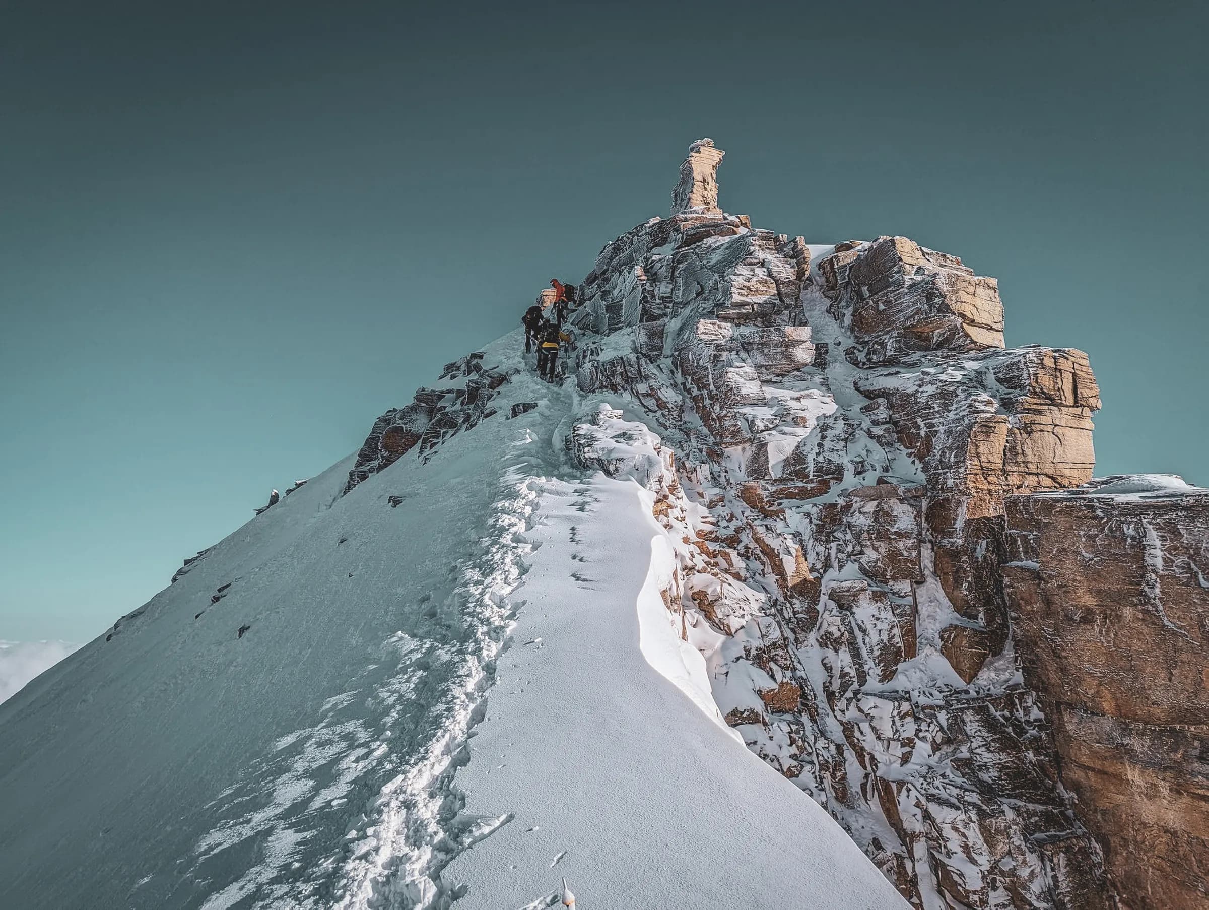 Trekking in the high mountains, on a snow-covered ridge with climbers against a backdrop of blue skies.