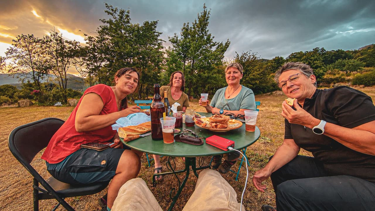 Four friends enjoy a convivial meal in the open air, with tasty food and a beautiful summer sky.