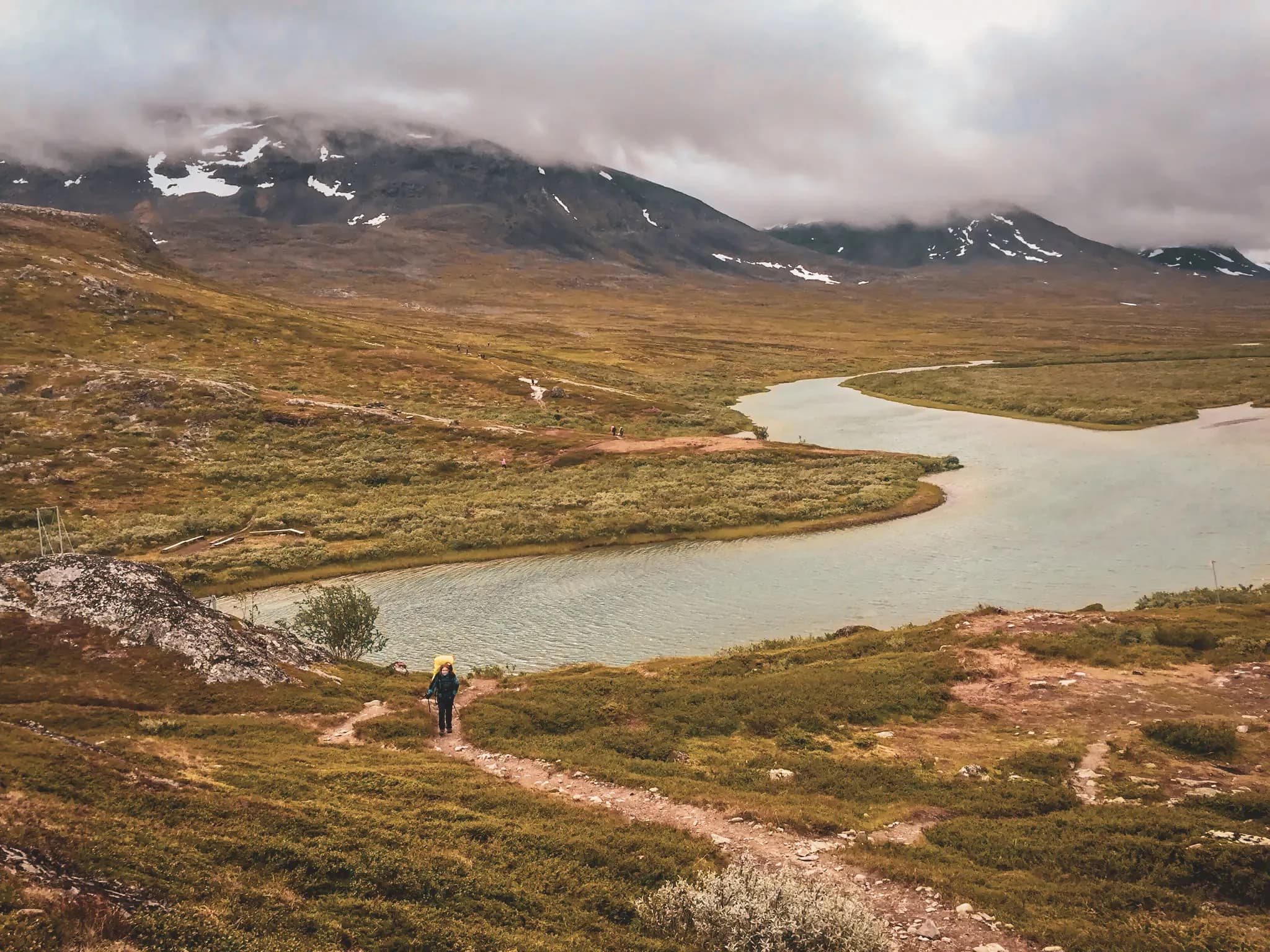 A hiker on a verdant path, revealing majestic mountains and sparkling liquid.