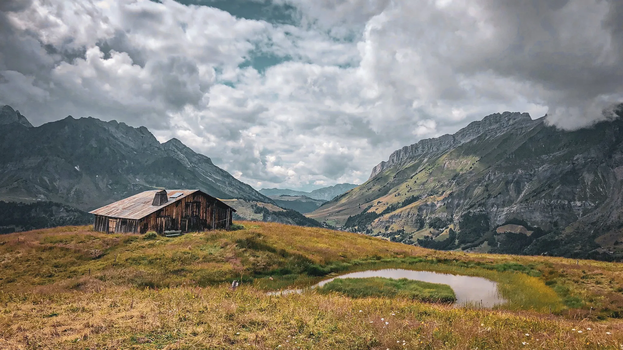 Une cabane rustique au milieu des prairies, avec des montagnes majestueuses en toile de fond.