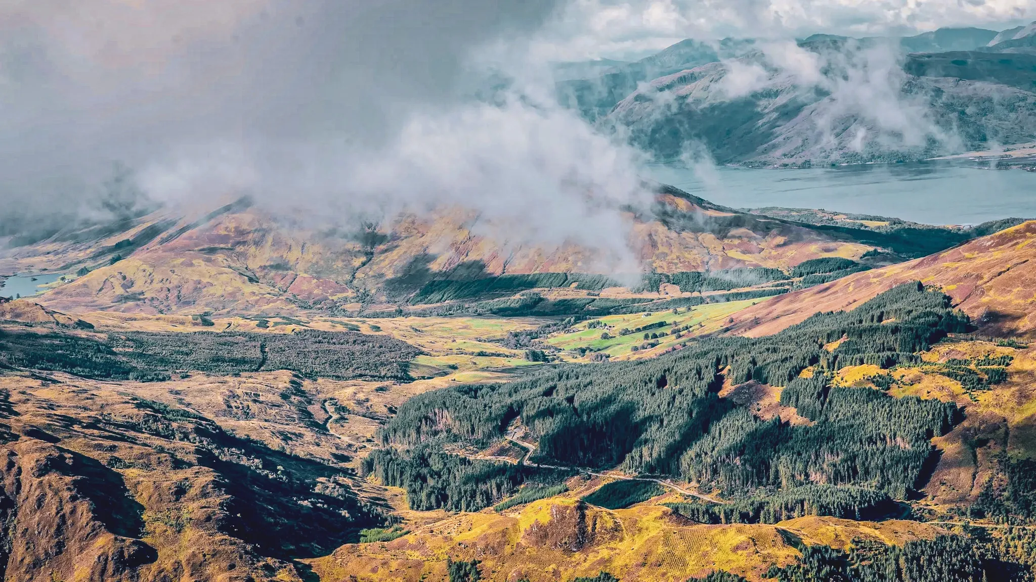 Een uitgestrekt panorama van de Schotse Hooglanden, waar bergen en valleien zich mengen in de wolken.