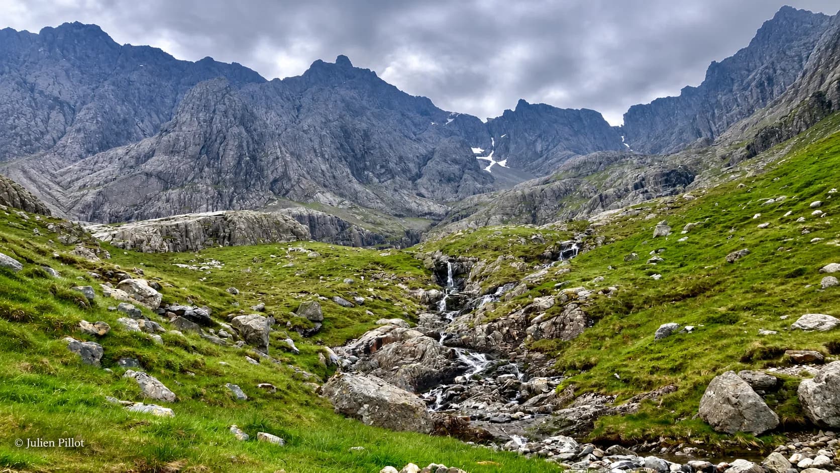 Een Schots berglandschap, met rotsachtige bergkammen, groene valleien en een kronkelend beekje.