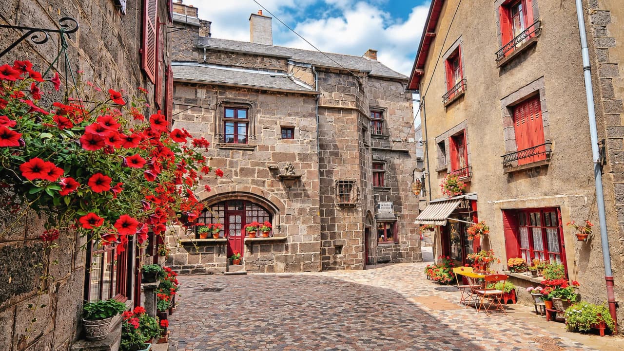Ruelle pittoresque avec des maisons en pierre, parsemée de fleurs colorées et d'une ambiance charmante.