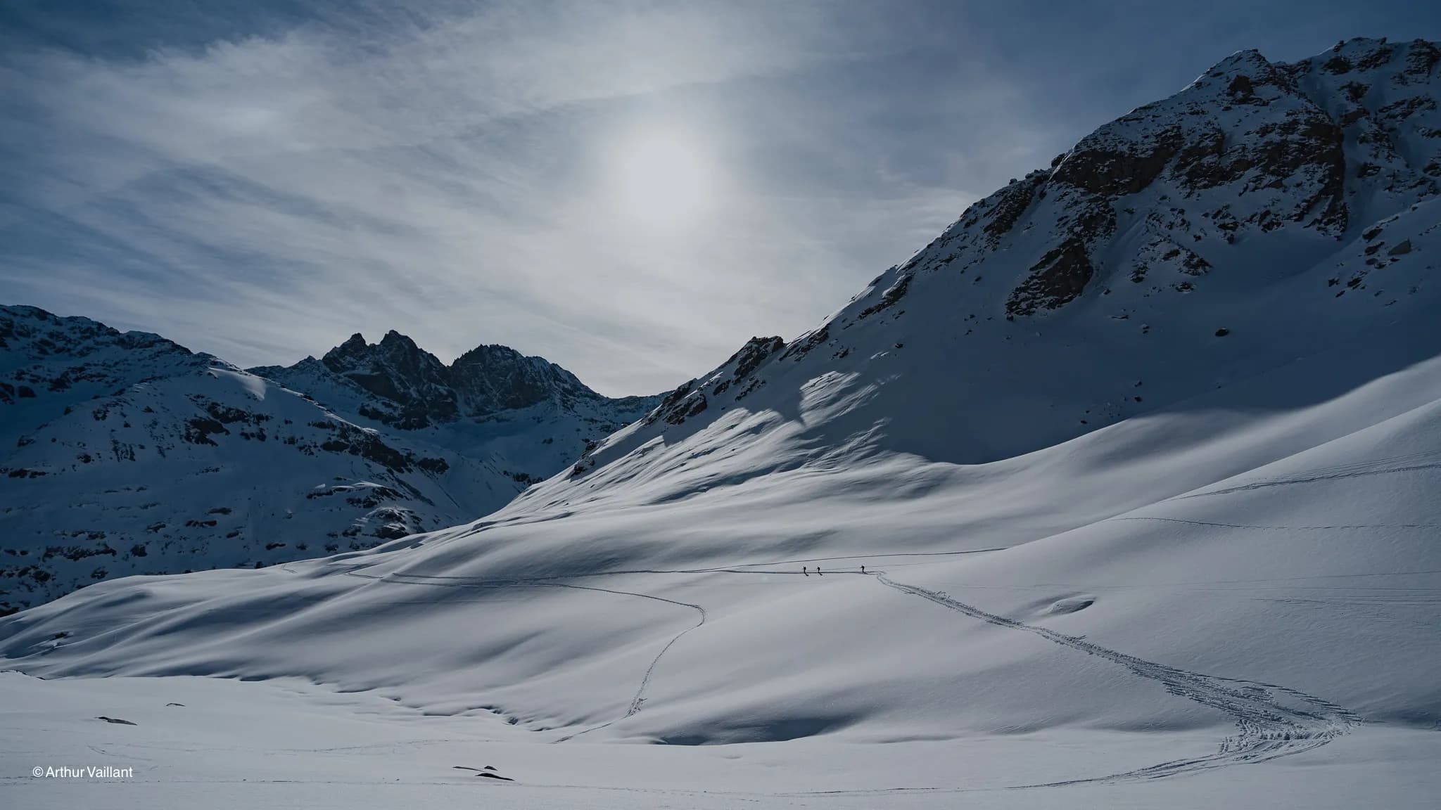 Spectacular alpine scenery, pristine snow, skiers on the high route, beneath a sunny sky.