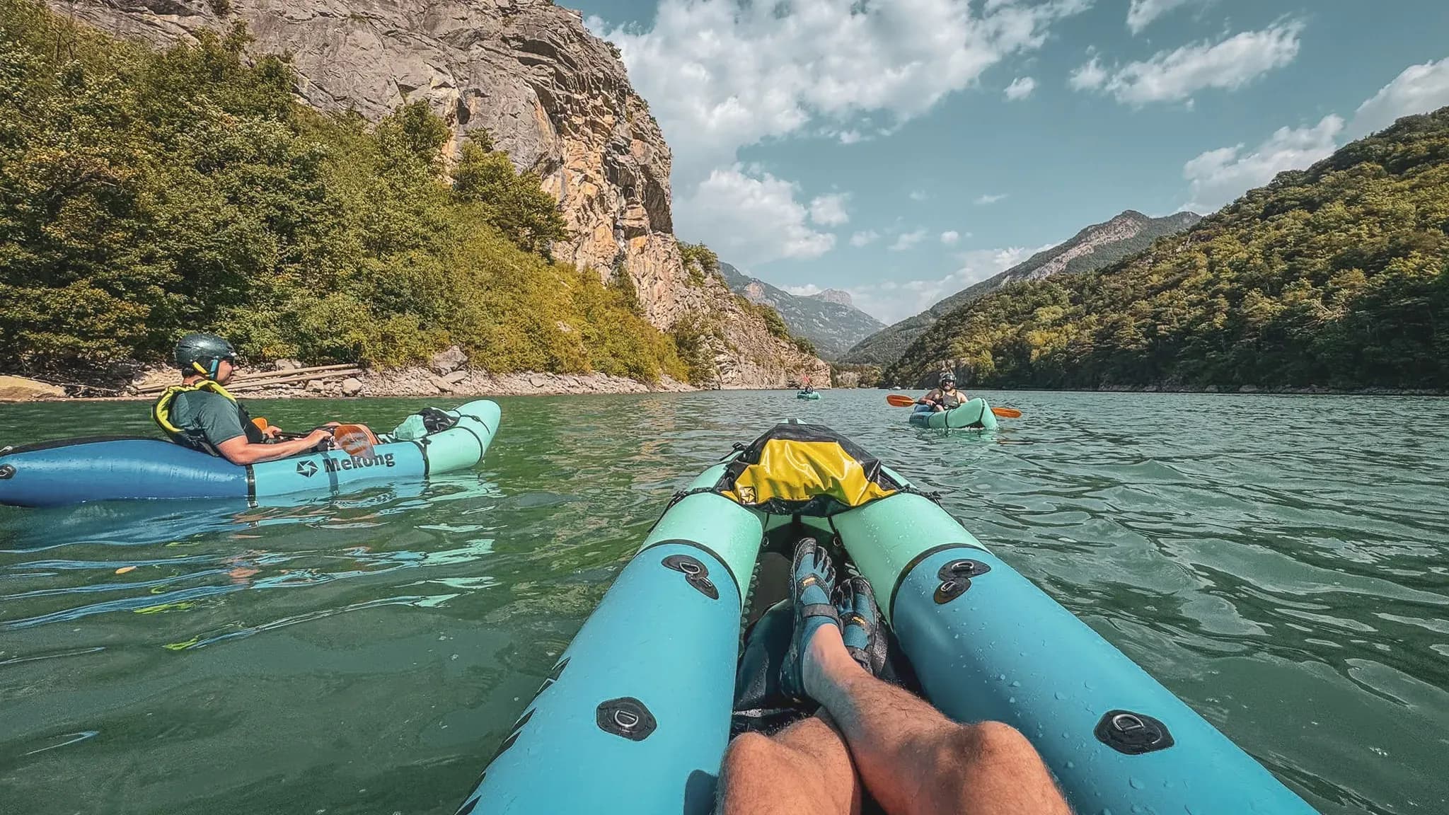 A group of packrafts gliding along an alpine river surrounded by green cliffs.