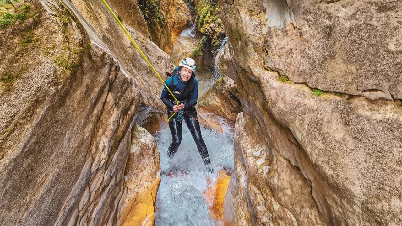 Participant souriant en canyoning, entouré de roches, éclats d'eau et nature vibrante.