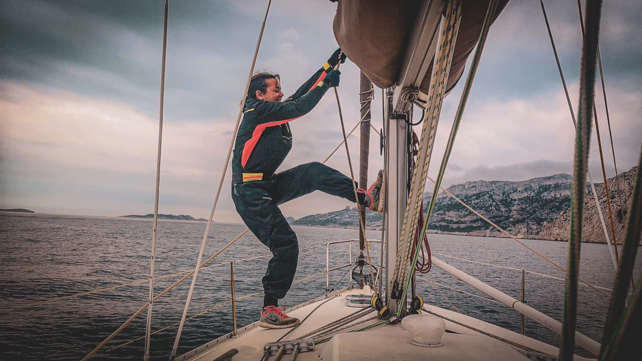 Navigateur s'élançant sur un voilier en Méditerranée, montagnes en arrière-plan. Aventure en mer !