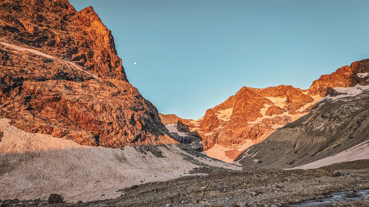 Montagnes majestueuses aux sommets dorés, ciel bleu et glacier paisible, invitation à l'aventure.