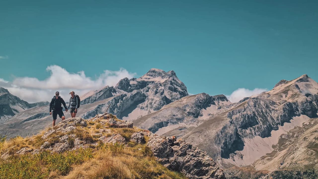 Een paar wandelaars op de top van een berg, met uitzicht op een spectaculair Alpenlandschap.