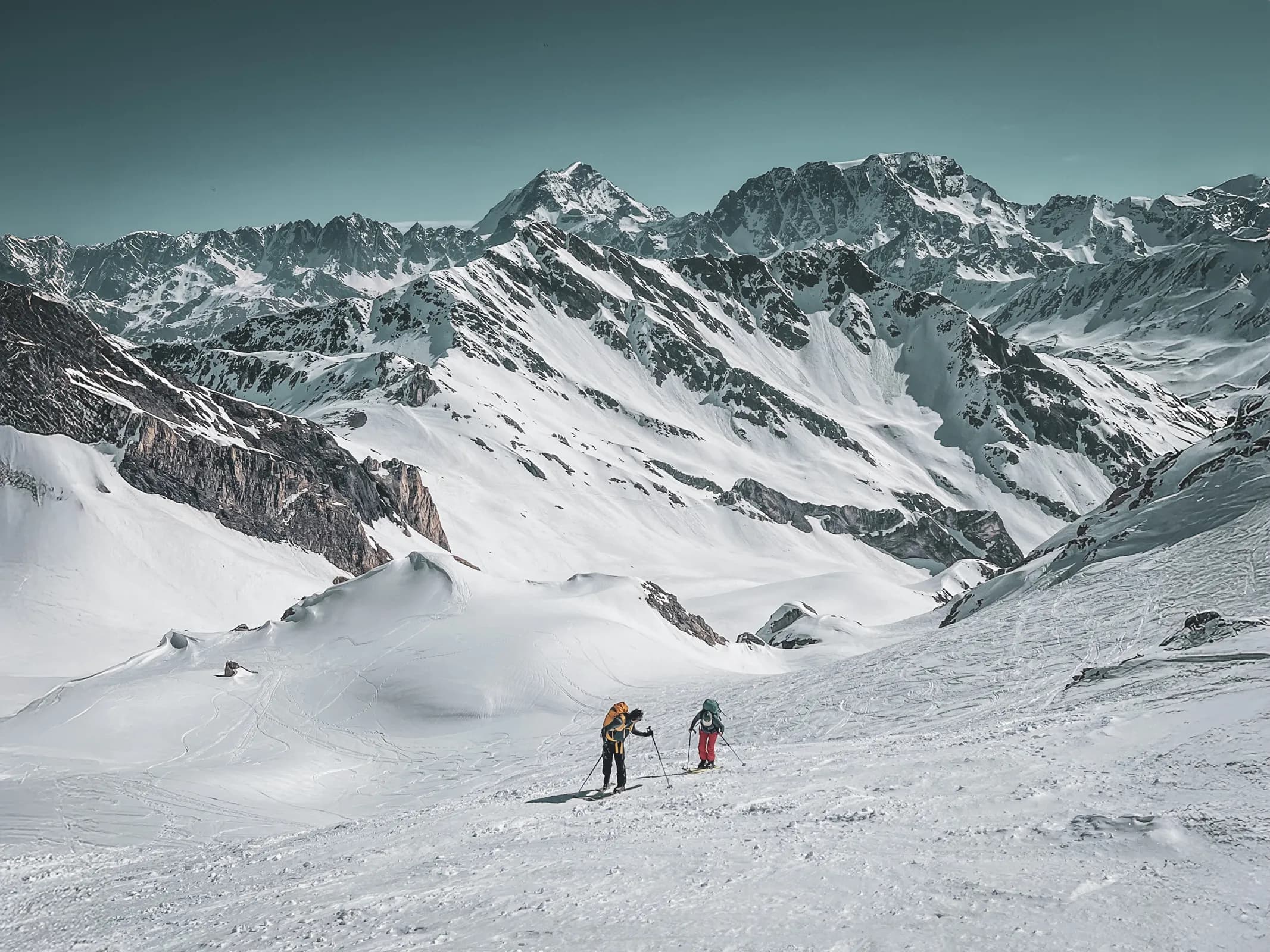 Deux skieurs en randonnée dans un paysage alpin enneigé, entourés de majestueuses montagnes.