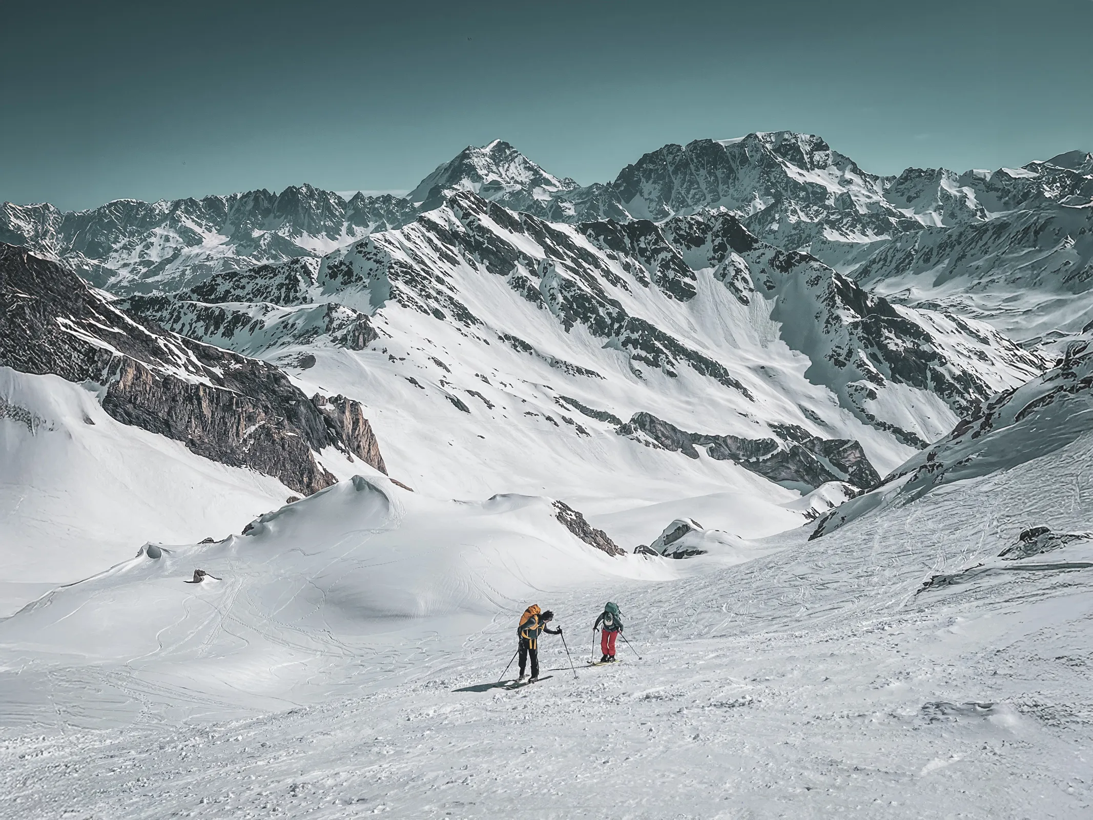 Deux skieurs en randonnée dans un paysage alpin enneigé, entourés de majestueuses montagnes.