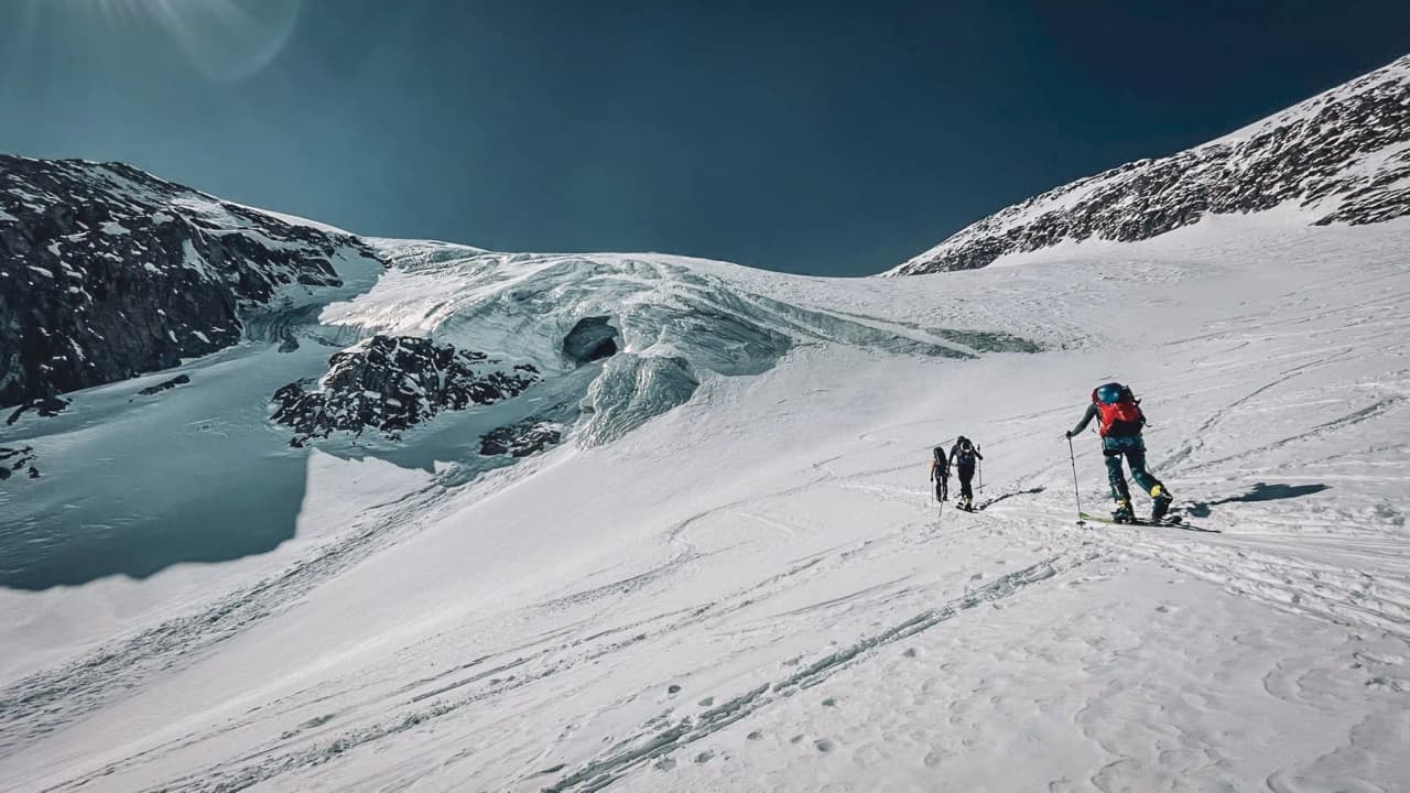 Breathtaking Alpine scenery with skiers crossing a glacier under a brilliant blue sky.