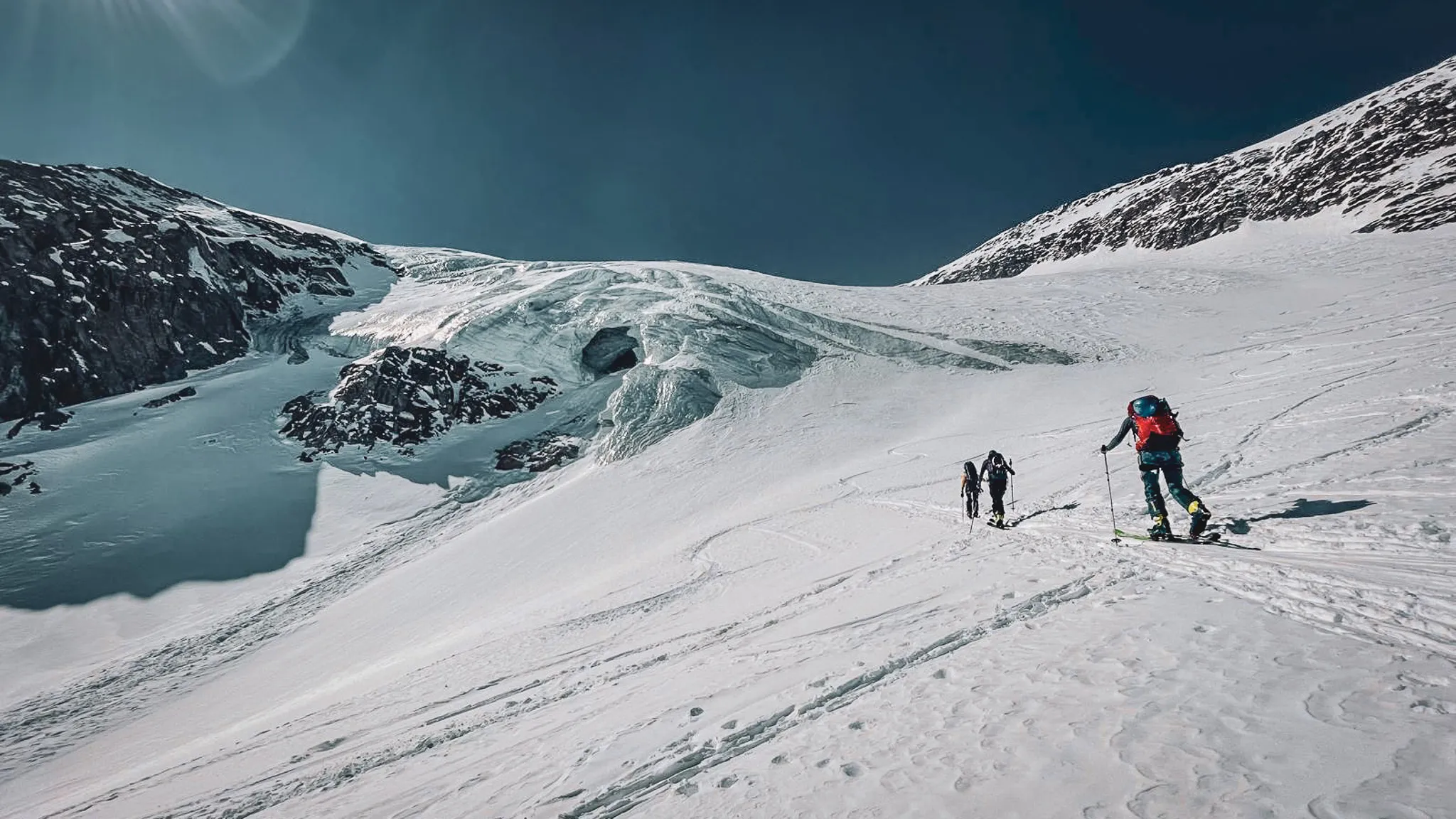 Paysage alpin époustouflant avec des skieurs traversant un glacier sous un ciel bleu éclatant.