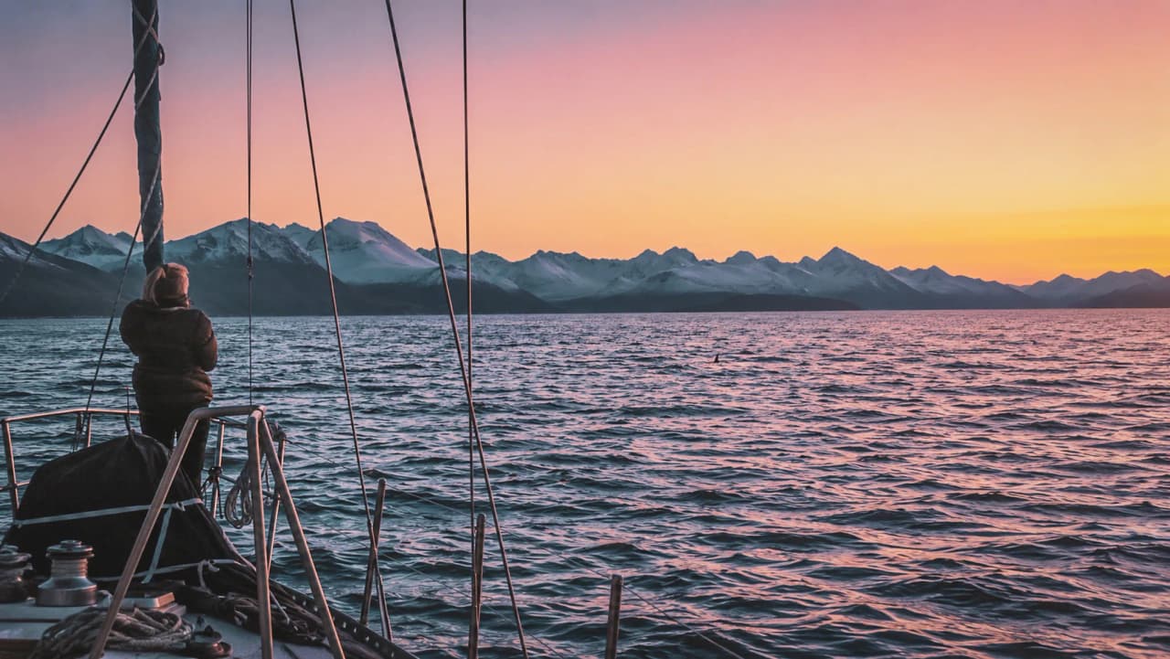Een zeiltocht bij zonsondergang, met uitzicht op majestueuze bergen in een fjord.