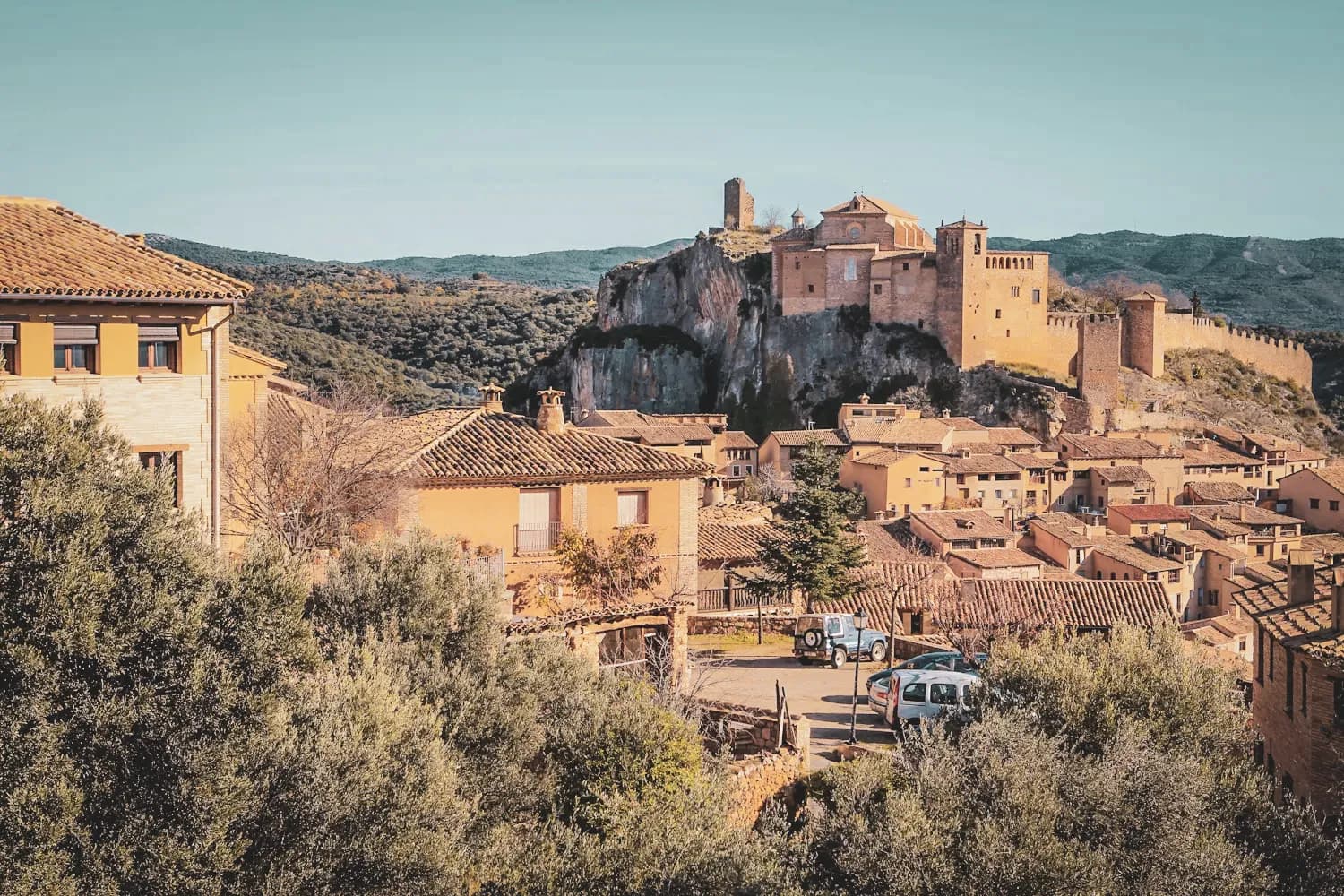 Picturesque view of a village with a medieval castle overlooking colourful houses and green hills.