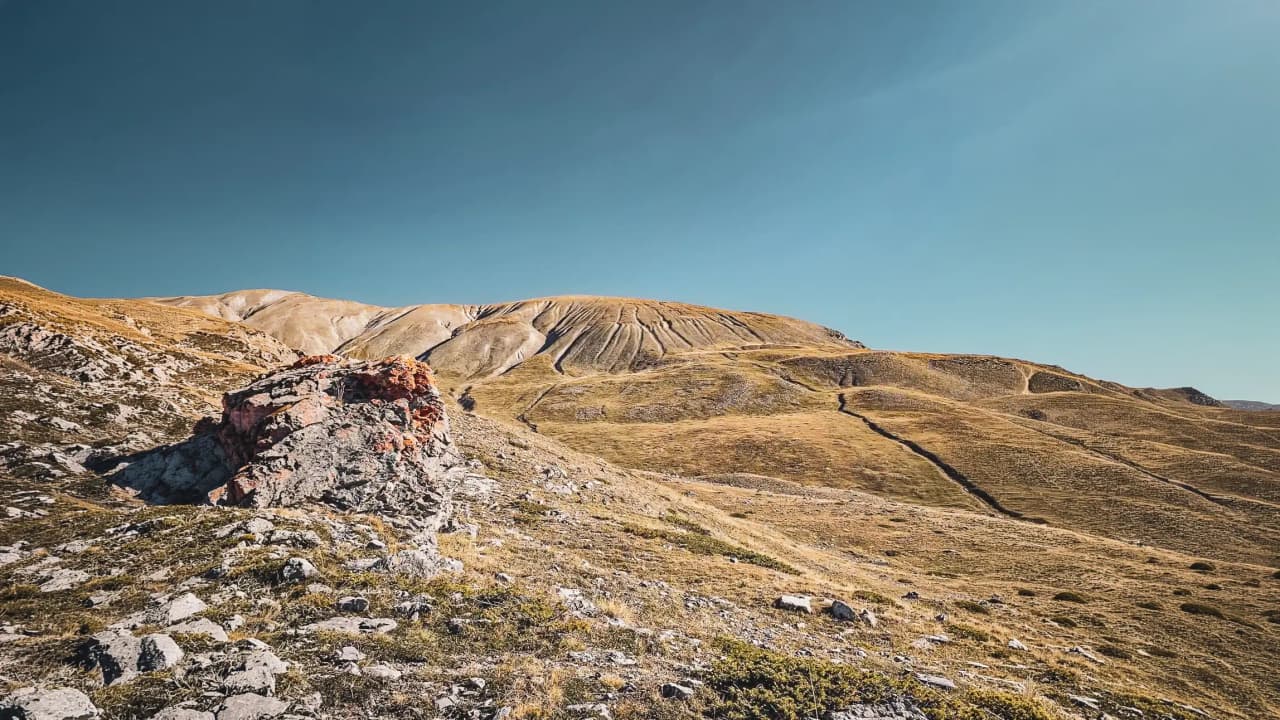 Gouden alpine domein onder een blauwe hemel, bezaaid met rotsen en wandelpaden.