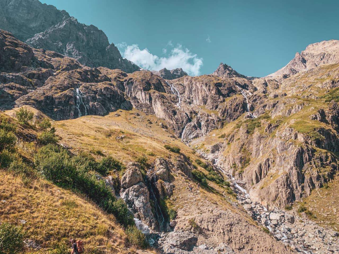 Paysage alpin spectaculaire avec des montagnes, des cascades et un ciel bleu éclatant.