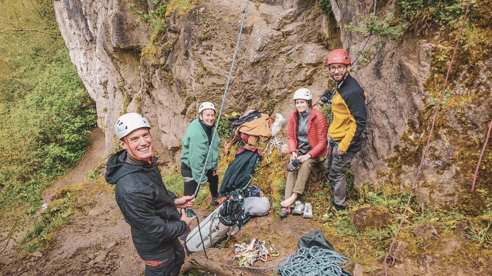 Groupe d'escaladeurs souriants préparant leur aventure en falaise, entourés de verdure.