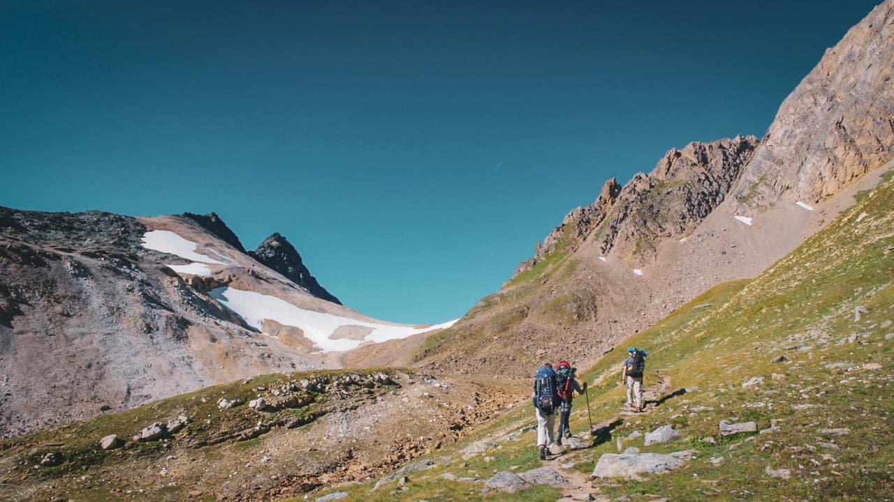 Randonneurs sur un sentier alpin, entourés de montagnes majestueuses et d'un ciel bleu éclatant.