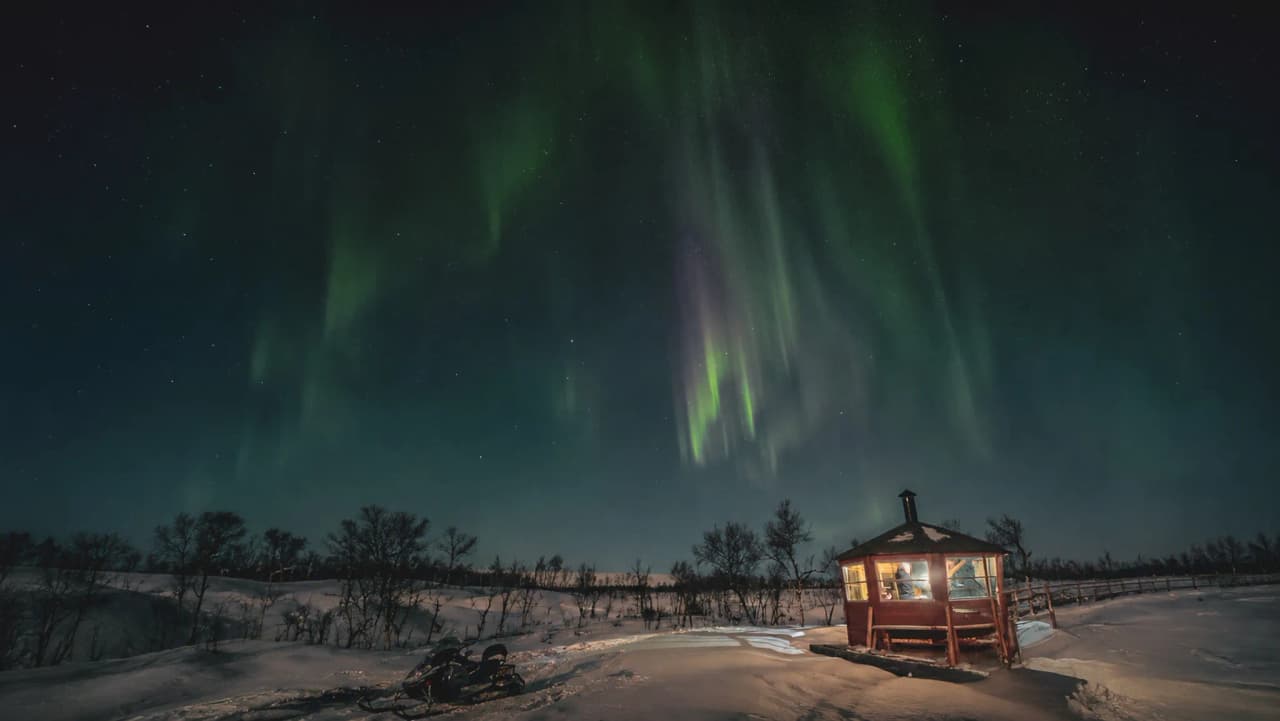 Sous un ciel étoilé illuminé par des aurores dansantes, un refuge chaleureux émerge de la neige.