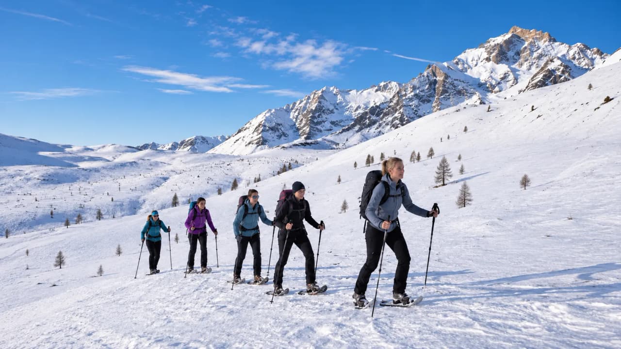 A group of women on snowshoes on a snow-covered path, with the majestic mountains in the background.
