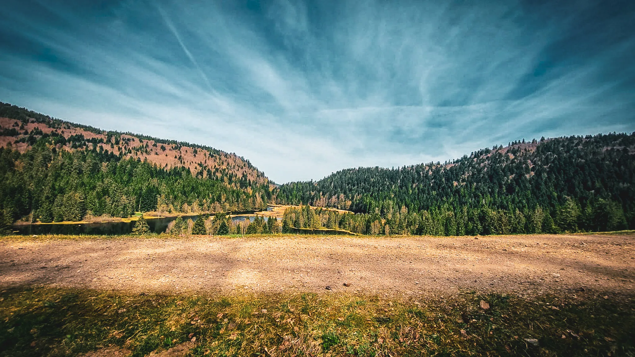 Paysage des Vosges avec lacs et forêts verdoyantes sous un ciel bleu, invitant à l'évasion.