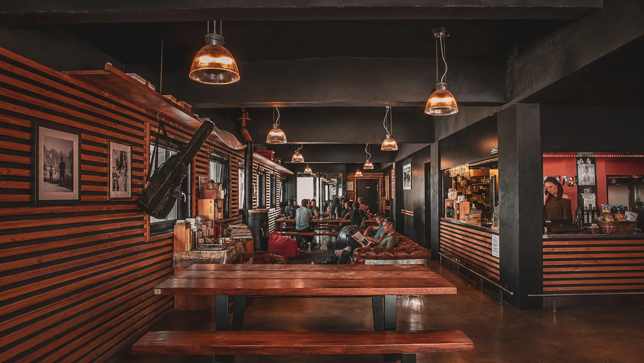 A cosy inn with wooden tables, hanging lights and relaxed travellers.