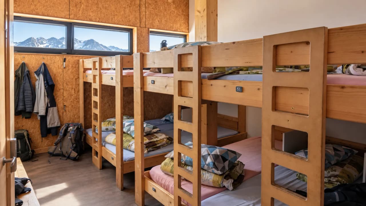 Slaapzaal in de berghut met houten stapelbedden, dekbedden en ramen met uitzicht op de bergen.