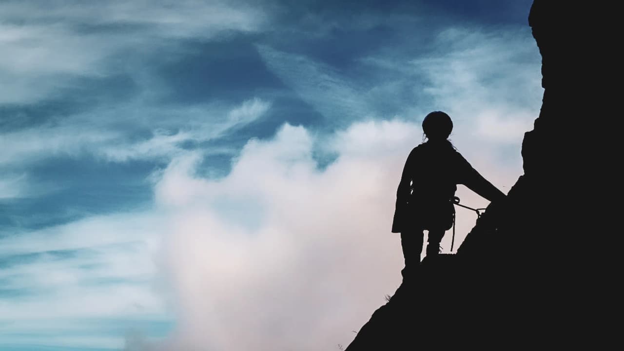 Het silhouet van een klimmer op de Mont Aiguille, heldere luchten, de belofte van avontuur en adembenemende panorama's.