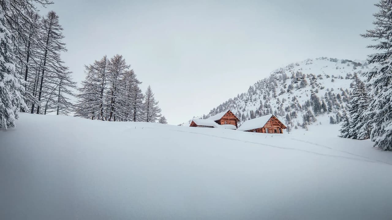 Mountain huts nestled in the heart of a snow-covered landscape, surrounded by fir trees beneath a peaceful winter sky.