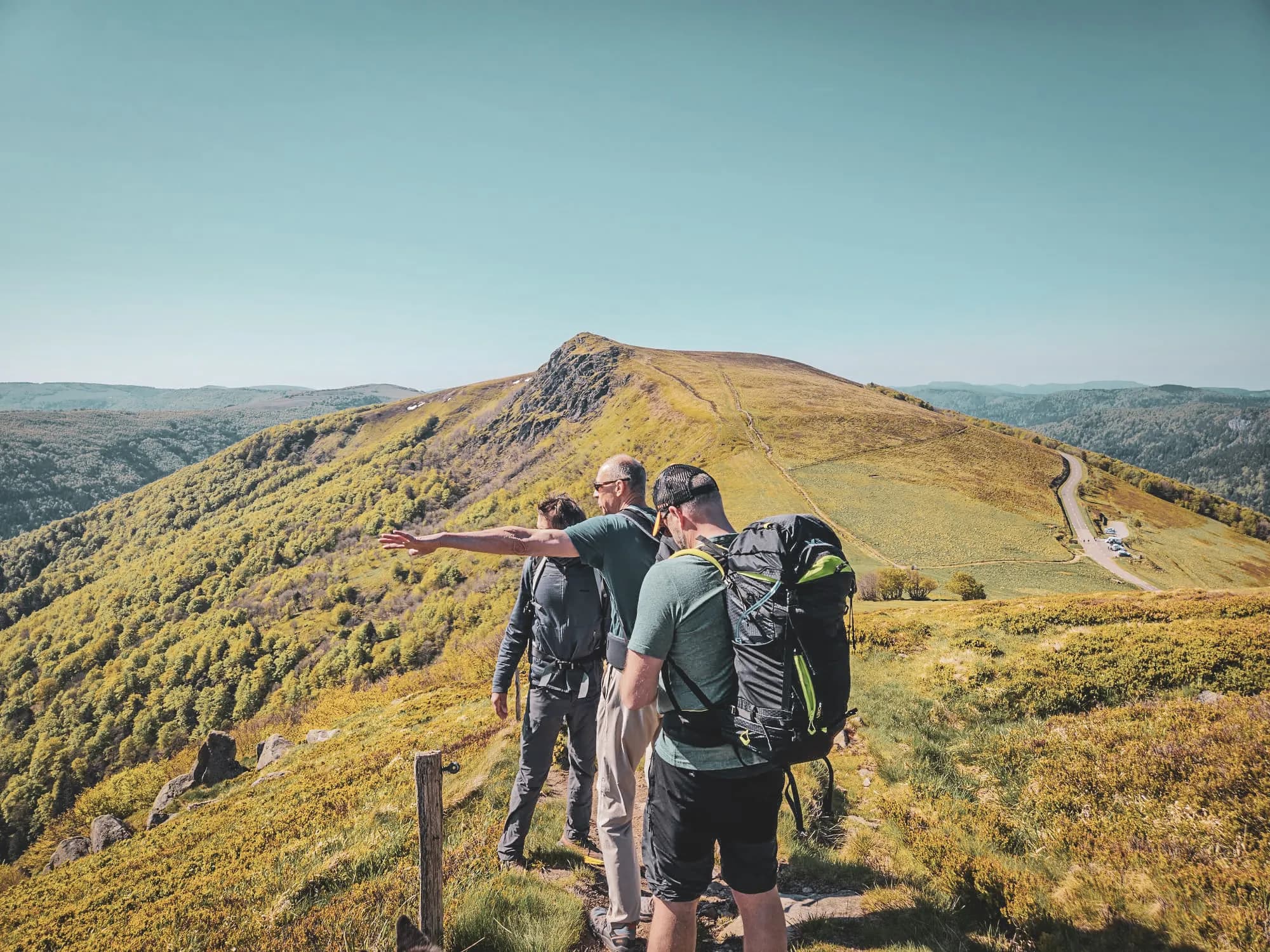 Trois randonneurs admirent un panorama verdoyant des Vosges sous un ciel bleu éclatant.