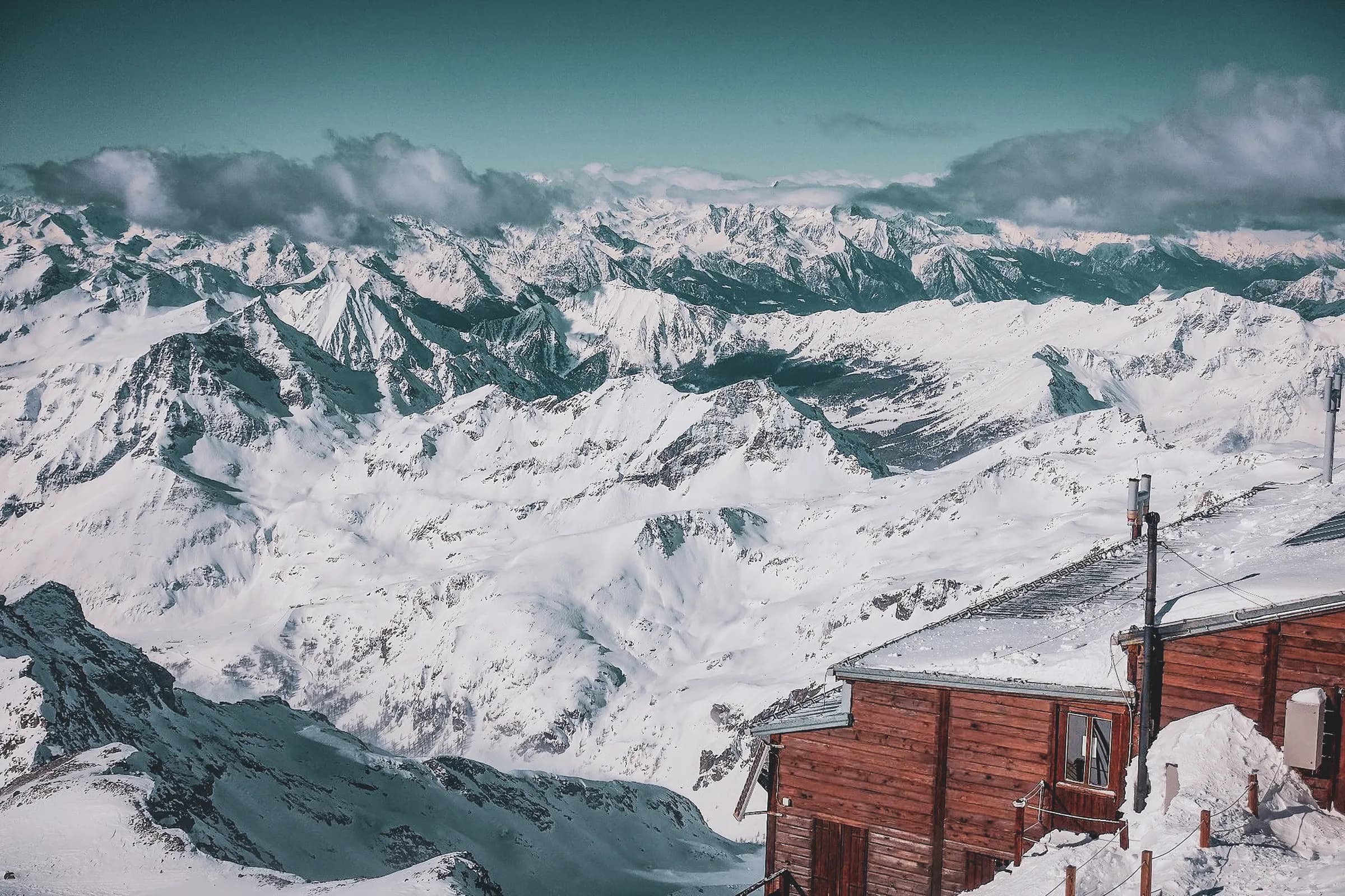 Vue panoramique des montagnes enneigées du Mont Rose, avec un refuge en bois accueillant.