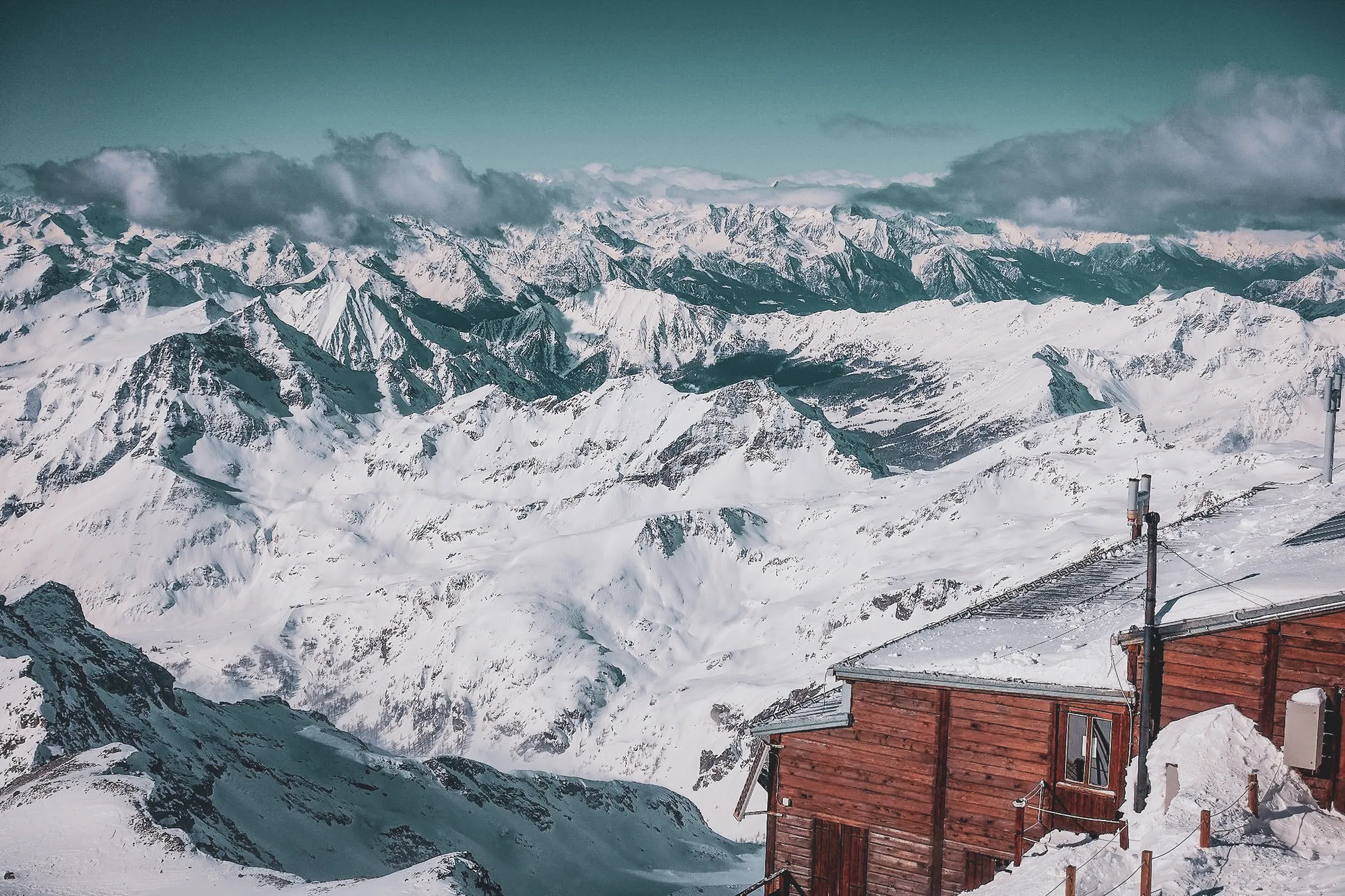 Vue panoramique des montagnes enneigées du Mont Rose, avec un refuge en bois accueillant.