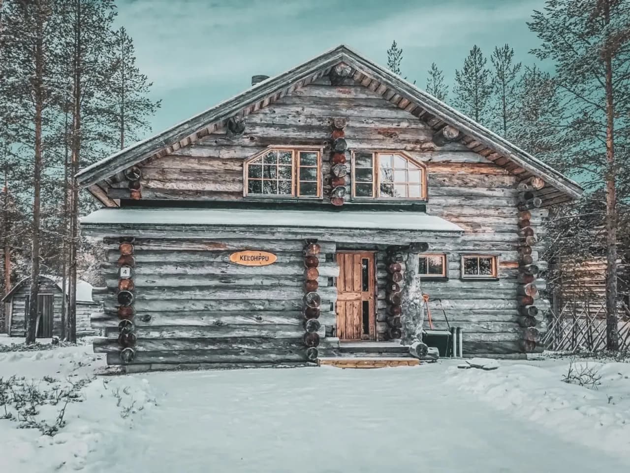 Maison en bois traditionnel en Laponie, entourée de neige, sous un ciel clair et apaisant.